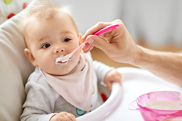 Image showing father feeding baby sitting in highchair at home