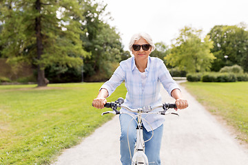 Image showing happy senior woman riding bicycle at summer park