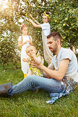 Image showing The happy young family during picking apples in a garden outdoors