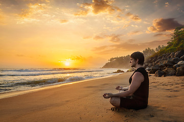 Image showing Young sporty fit man doing yoga meditating on tropical beach