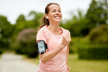 Image showing woman with earphones add armband jogging at park