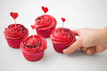 Image showing close up of hand taking cupcakes with heart sticks