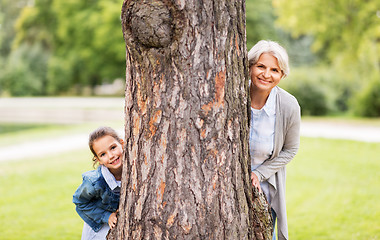 Image showing grandmother and granddaughter behind tree at park