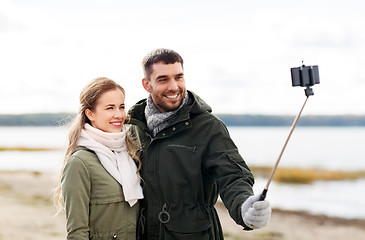 Image showing happy couple taking selfie on beach in autumn