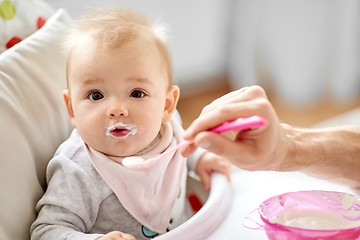 Image showing father feeding baby sitting in highchair at home