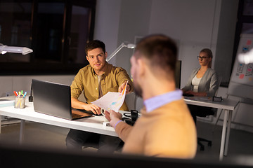 Image showing man giving papers to colleague at night office