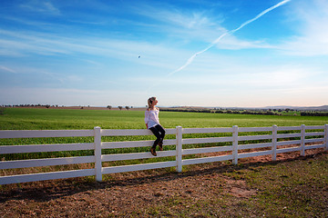 Image showing Woman sitting on white farm fence in rural fields