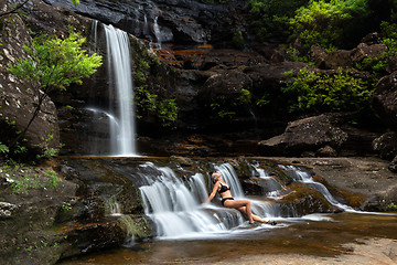 Image showing Woman sitting in flowing waterfall cascades immersed in nature oasis