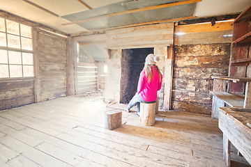 Image showing Woman sitting inside an old timber hut on log stools Snowy Mountains