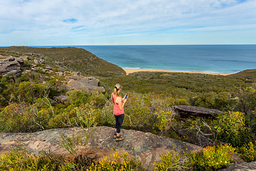 Image showing Woman on clifftop holding mobile phone, views to ocean beach