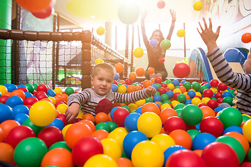 Image showing young mom playing with kids in pool with colorful balls