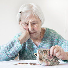 Image showing Elderly woman sitting at the table counting money in her wallet.