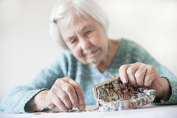 Image showing Concerned elderly woman sitting at the table counting money in her wallet.