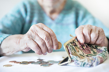 Image showing Detailed closeup photo of unrecognizable elderly womans hands counting remaining coins from pension in her wallet after paying bills.