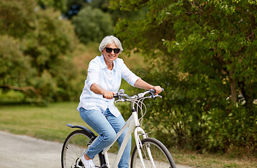 Image showing happy senior woman riding bicycle at summer park