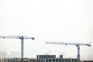 Image showing Building under construction with two tower cranes against a gray cloudy sky.