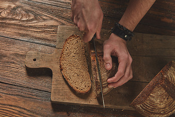 Image showing fresh bread cut man\'s hands on wooden board