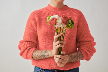 Image showing A beautiful bouquet of flowers of a Ranunculus in a girl\'s hands with tatoo on a gray background. Trend color of the year 2019 Living Coral Pantone. Place for text.