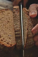 Image showing young man\'s hand cut fresh dark bread