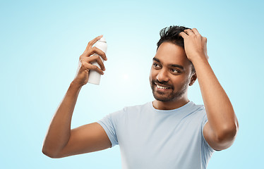 Image showing smiling indian man applying hair spray over gray