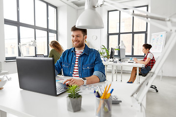 Image showing smiling creative man with laptop working at office