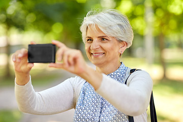 Image showing senior woman photographing by cell at summer park