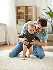 Image showing father helping baby daughter with walking at home