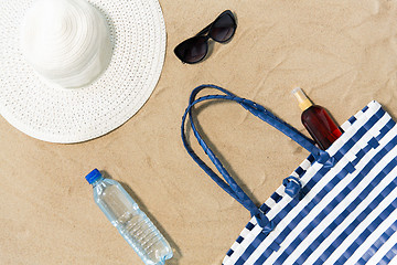 Image showing beach bag, sunscreen, sunglasses and hat on sand