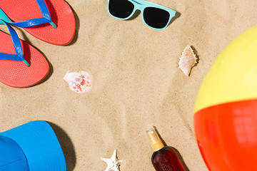 Image showing cap, flip flops and shades and beach ball on sand