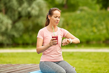 Image showing woman with smoothie looking at smart watch in park