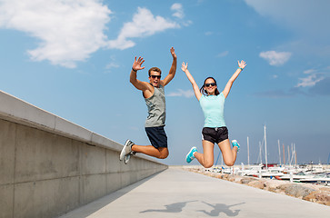 Image showing happy couple in sports clothes jumping on pier