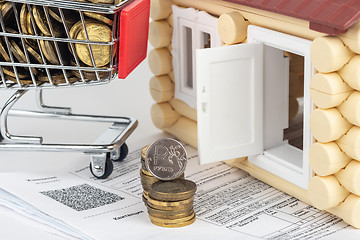 Image showing A cart with money, a stack of money and a coin of one ruble in the bills for an apartment, in front of the door to the house