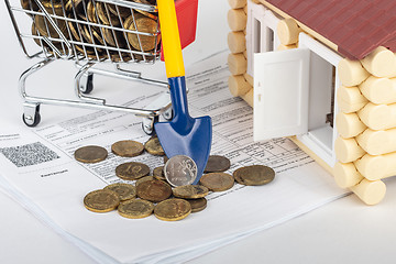 Image showing A shovel with a ruble coin rests on a money cart, a number of apartment bills and a toy house