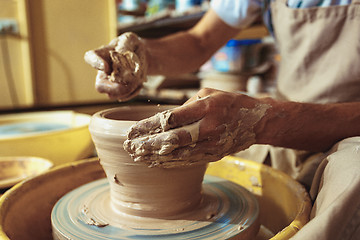 Image showing Creating a jar or vase of white clay close-up. Master crock. Man hands making clay jug macro.