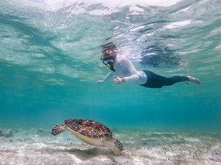 Image showing Woman on vacations wearing snokeling mask swimming with sea turtle in turquoise blue water of Gili islands, Indonesia. Underwater photo.