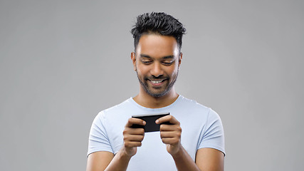 Image showing happy indian man playing game on smartphone