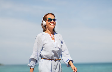 Image showing woman with headphones walking along summer beach