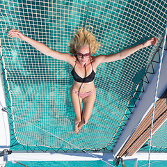 Image showing Woman relaxing on a summer sailing cruise,lying in hammock of luxury catamaran near picture perfect white sandy beach on Spargi island in Maddalena Archipelago, Sardinia, Italy.