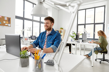 Image showing smiling creative man with laptop working at office