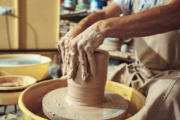 Image showing Creating a jar or vase of white clay close-up. Master crock. Man hands making clay jug macro.