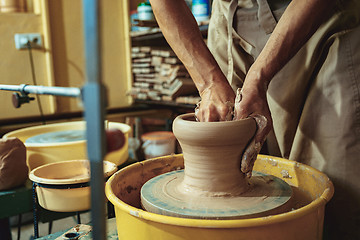 Image showing Creating a jar or vase of white clay close-up. Master crock. Man hands making clay jug macro.