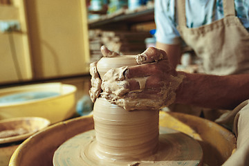 Image showing Creating a jar or vase of white clay close-up. Master crock. Man hands making clay jug macro.