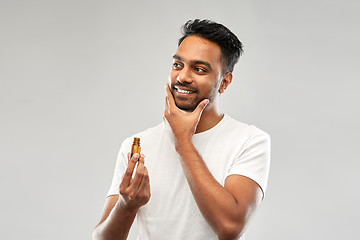 Image showing smiling indian man applying grooming oil to beard