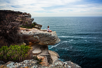 Image showing Relaxed woman sitting on coastal headland looking out to ocean