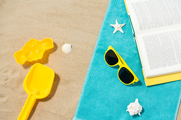 Image showing sunglasses, sand toys and book on beach towel