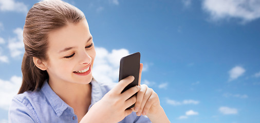 Image showing smiling girl messaging on smartphone over blue sky