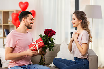 Image showing happy man giving woman flowers and present at home