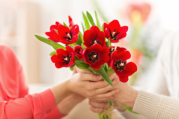 Image showing close up of man giving red tulip flowers to woman