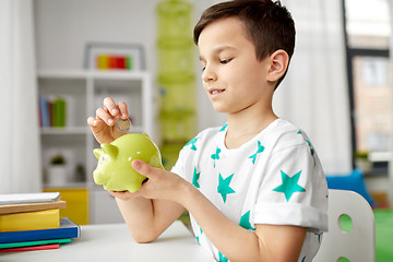 Image showing little boy putting coin into piggy bank at home