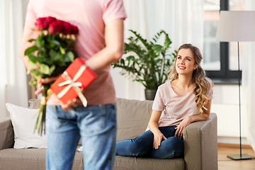 Image showing woman looking at man with flowers and gift at home